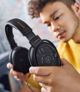 Casque audio Sennheiser HD 660S2 noir tenu par une main, porté par un jeune homme souriant au teint mat et aux cheveux bouclés