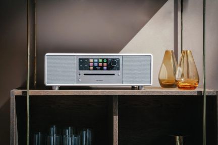 Бял компактен hi-fi уред на дървен рафт, два кехлибарени стъклени вази от двете страни
