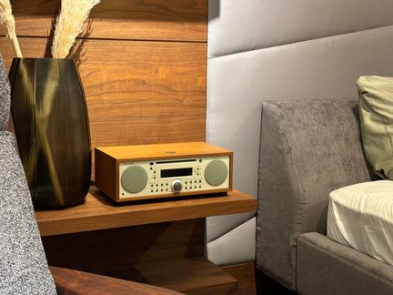 Lyst træradio med cremefarvet front, to runde højttalere, skærm og knapper, set i trekvartsprofil på hylde