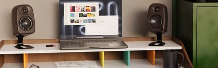 Íróasztal nyitott laptoppal két fekete monitorhangfal között, fekete csésze az előtérben