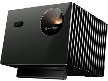 Vidéoprojektorius Valerion VisionMaster Pro 2 juodas, su blizgiu stiklo priekiniu fasadu, apvaliu objektyvu ir mažu jutikliu, dešinysis šonas su vertikaliomis metalinėmis grotelėmis, vaizdas iš dešinės priekinės pusės trimis ketvirčiais