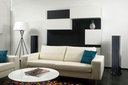 Modern living room with beige sofa, teal cushions, colorful rug, black and white wall shelves, decorative vase