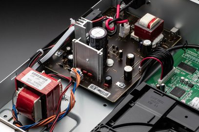 Sisäkuva hopeisesta Denon DCD-900NE CD-soittimesta, jossa näkyvät elektroniset komponentit, muuntajat ja piirilevyt