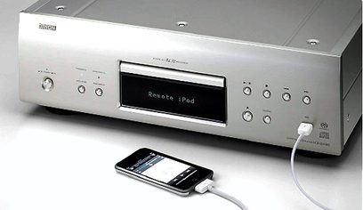 Ezüstszínű Denon DCD-2010 CD-lejátszó elölnézetből, kijelzővel, gombokkal és vezérlőkkel, fekete mobilkészülékhez csatlakoztatva