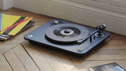 Black turntable on wooden floor, with colorful vinyl records and metallic tonearm