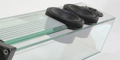 Gennemsigtig glassøjle med to ovale sorte højttalere på en rektangulær sort og grå base