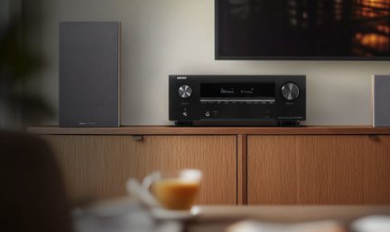 Svart metall A/V-forsterker, front med sentralt skjerm og to knapper, forfra sett, på trebord