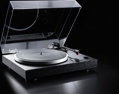 Hi-Fi-Plattenspieler Dual CS 518 aus Dreiviertelansicht, rechteckiges Gehäuse aus strukturiertem schwarzem Holz, silberfarbener Aluminium-Plattenteller mit schwarzer Gummimatte, hochgeklappte transparente Abdeckung, gerader grauer Tonarm mit rotem Tonabnehmer, kleiner schwarzer Knopf an der rechten Frontseite