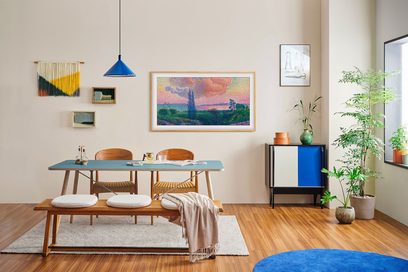 Samsung F-TQ55LS03D-BF indrammet højdefinitions-tv, rektangulært blåt bord, 2 træstole, træbænk, blå pendel, gråt tæppe, grønne planter, sort og blå skænk, beige væg, farverige vægdekorationer