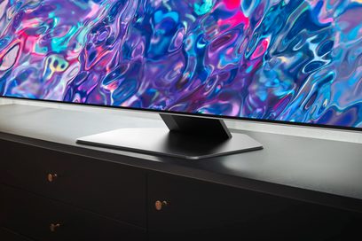 Televizor Samsung QE55QN85B 2022 zobrazující barevný abstraktní obraz na své obrazovce, umístěný na černém nábytku