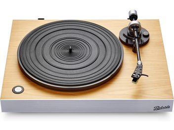 Drewniany gramofon hi-fi Roberts Stylus Luxe w jasnym kolorze z aluminiową, srebrną frontową obudową, czarnym, żłobionym talerzem oraz ramieniem odtwarzającym w kolorze czarno-srebrnym, okrągłym przyciskiem prędkości 33/45 obrotów, widocznym logo na froncie, widok z góry lekko z perspektywy