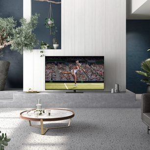 Panasonic TX-75JX940E-fladskærms-tv, der viser en kvindelig tennisspiller i aktion på en bane under en kamp, i et moderne stuelokale