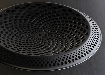 Close-up frontal view of a black circular speaker, with a metal grille perforated with concentric holes
