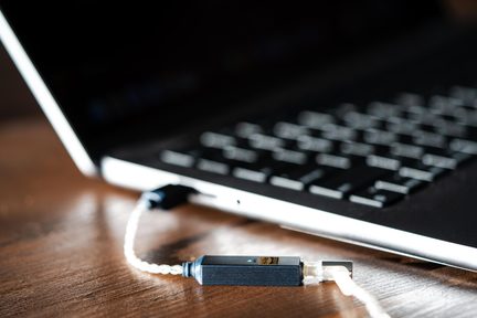 Ahşap masanın üzerinde gümüş renkli bir dizüstü bilgisayara bağlı siyah taşınabilir USB DAC ses adaptörü