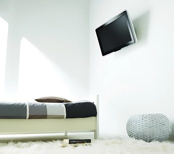 Vogel's EFA 8810 vægbeslag til TV i hvid metal, monteret på væggen, med sort fladskærm, hvid seng og grå og sorte puder