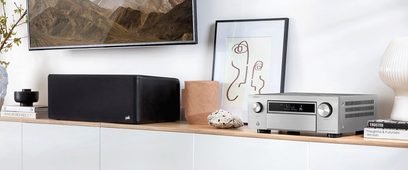 Denon AVC-X6700H sølvfarvet hjemmebiografsforstærker, set forfra, placeret på et lyst trækabinet sammen med andet hi-fi-udstyr