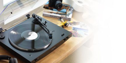 Sort vinylpladespiller i sort plast og metal, åbent låg, roterende plade, trekvartsvisning på træbord