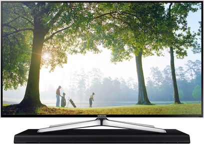 Televizor Samsung zobrazující obrázek čtyř osob v mlhavém lesním parku, umístěný na černém soundbaru