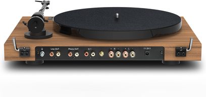 Hi-Fi vinila atskaņotājs Pro-Ject Juke Box E1 riekstkoka apdarē, aizmugures skats, taisnstūrveida pamatne ar koka apdari, redzami RCA savienotāji un barošanas pieslēgums.