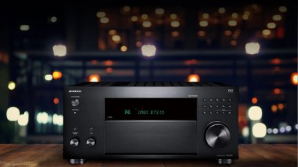 Černý audio-videoreceiver Onkyo TX-8250, pohled zepředu, položený na dřevěném stole v tmavé místnosti s rozmazanými světly v pozadí