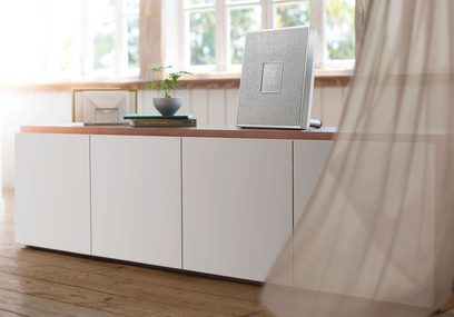 Trådløs, tilsluttet Yamaha ISX-80 højttaler i hvid på hvidt møbel, set forfra, med grøn plante og bøger ved siden af