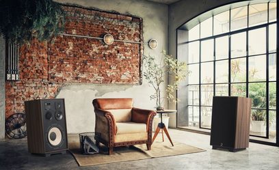 Interiér ve stylu loftu s cihlovou zdí, okny s mřížemi, vintage koženým křeslem a stolem, dřevěnými hi-fi reproduktory