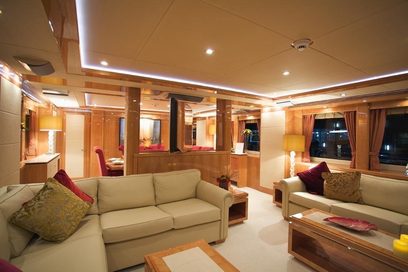 Luksuriøst yachtinteriør med beige sofaer, bordeauxrøde puder, træbordplader, beige tæppe og store vinduer