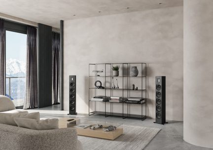 Moderne stue med beige sofa, lys træ sofabord, sort metalreol, 2 sorte højttalere, stort vindue med gardiner