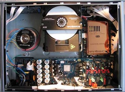 Vnitřek černého CD přehrávače Cambridge Audio 740C s viditelnými elektronickými součástkami, tištěnými spoji, kabely a mechanismy