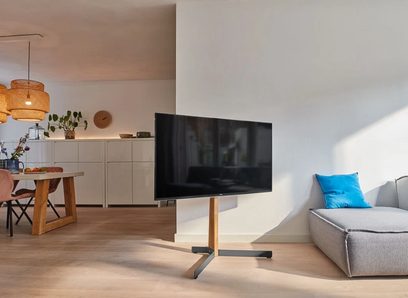 Wspornik ścienny na telewizor Vogel's TVS 3695, jasne drewniane wykończenie w odcieniu dębu, czarny płaski ekran, metalowa centralna podstawa, w nowoczesnym salonie
