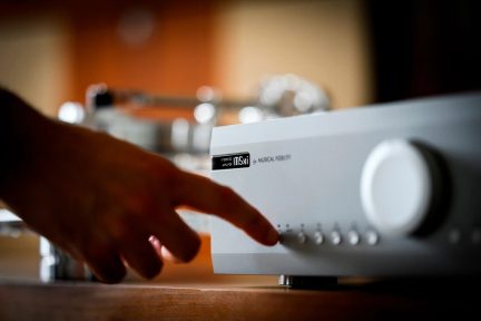 Sølvfarvet Musical Fidelity M5si hi-fi-forstærker, hånd der justerer frontpanelknapperne og stor lydstyrkeknap