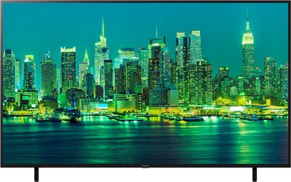 Panasonic TX-65LX700E-fladskærm, der viser et natligt vue af oplyste skyskrabere, der spejler sig i vandet