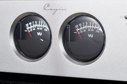Close-up van de zilverkleurige aluminium behuizing van de Cayin HA-2A high-fidelity hoofdtelefoonversterker, voorzien van twee ronde analoge VU-meters met naald.