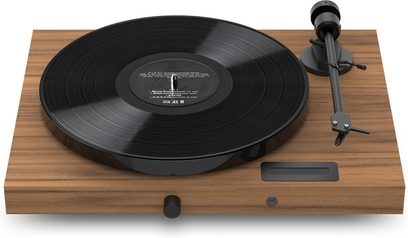 Hi-fi vinila atskaņotājs Pro-Ject Juke Box E1 riekstkoka apdarē ar melnu apaļu disku, melnu tonarmu, rotējošu pogu un taisnstūra pamatni
