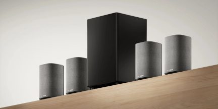 Sistem home cinema Loewe cu subwoofer negru și patru difuzoare gri pe raft din lemn