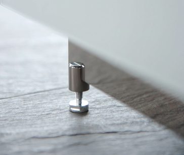 Cylindrisk, kromet metalfod til møbler, set fra siden, placeret på en lys, tekstureret træoverflade