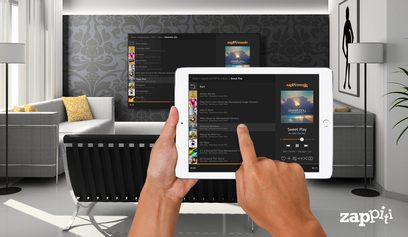 Tablet der viser Zappiti-brugergrænsefladen på en skærm med en musikliste, holdt af to hænder