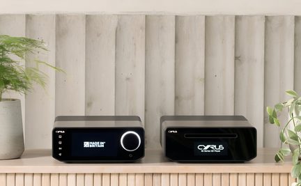 Two black metal audio devices, front view, screen and large illuminated knob on the left, CD slot and screen on the right