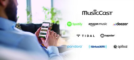 Bărbat văzut din spate pe canapea ținând smartphone controlând MusicCast și serviciile Spotify, Amazon Music, Deezer, Tidal, Qobuz