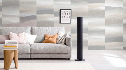 Zwarte torenventilator op voet in een moderne woonkamer met grijze bank en grijs-beige geometrisch behang