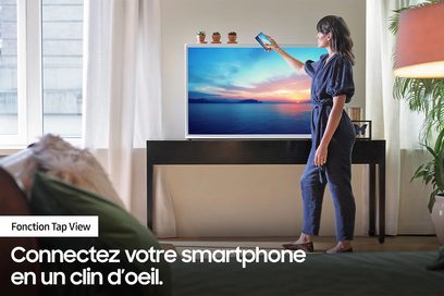 Samsung The Serif QE65LS01BB 2022 fladskærms-tv, der viser en solnedgang over havet, set forfra, kvinde der bruger en smartphone