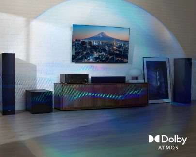 Moderní obývací pokoj s televizí na stěně, dřevěným nábytkem, černými reproduktory, zesilovačem, bílou lampou a opřeným obrazem