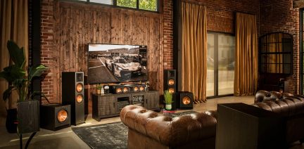 Living room with brown leather sofa, flat-screen TV, black speakers, wooden TV stand, golden curtains, red brick wall