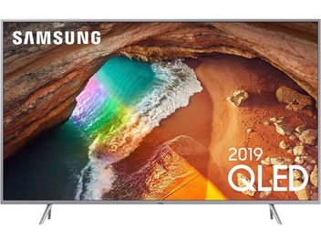 Samsung QE55Q64R-fladskærms-TV, der viser et farverigt luftfoto af en strand og en havgrotte, fladskærm på metalfod
