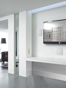 Moderní bílý interiér s nástěnnou televizí, barevným obrazem, prosklenými dveřmi a dekorativními lištami na stropě a stěně