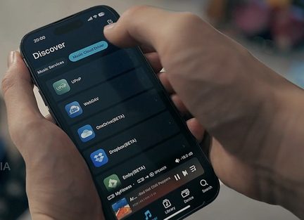 Črn pametni telefon iz stekla in kovine, z vklopljenim zaslonom na dotik, ki prikazuje vmesnik za glasbene storitve v oblaku, držan v roki, bližnji pogled pod kotom