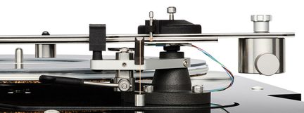 Nærbillede fra siden af en sølvfarvet metal-tonearm på en pladespiller, monteret på en sort, tekstureret base, med matchende cylindrisk kontravægt og fine, synlige flerfarvede kabler