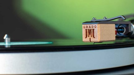 Gramofonová přenoska ze světlého dřeva s gravírováním „GRADO“, boční detailní záběr na raménko gramofonu a černou vinylovou desku
