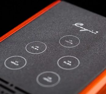 Nærbillede af den øverste plade i sort, tekstureret metal på Cayin HA-1A MK2 hovedtelefonforforstærkeren, indrammet af blanke rød-orange sider, med seks hvide, serigraferede cirkler og Cayin-logoet