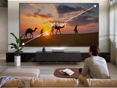 Samsung The Premiere SP-LSP7TFA videoprojektor, der projicerer et billede af 4 personer og 3 kameler i en ørken ved solnedgang på en 90 til 120 tommer skærm i en moderne stue